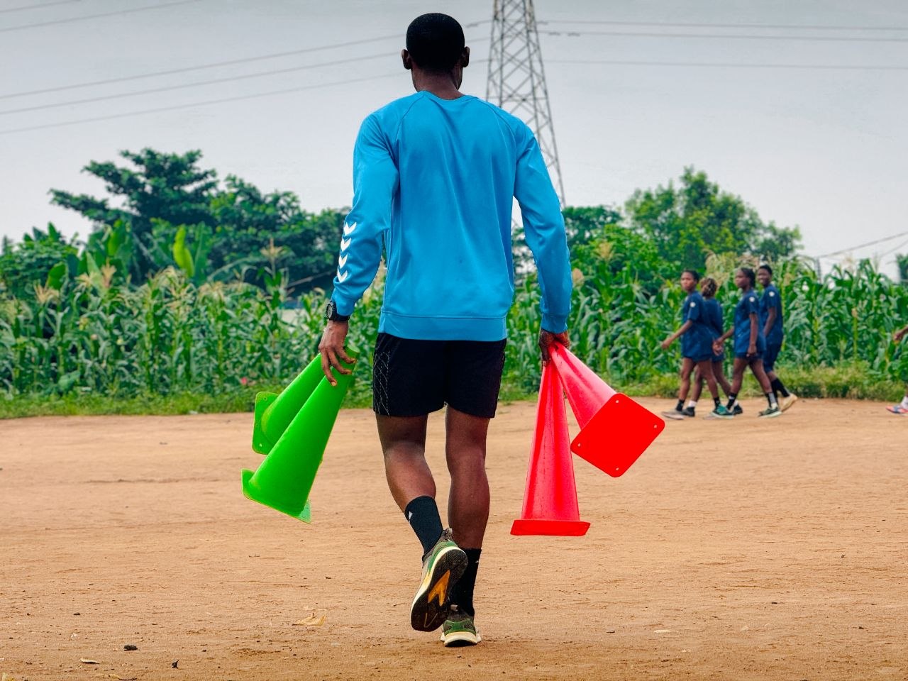 A BlueWhale coach carries training cones across the pitch while players train in the background