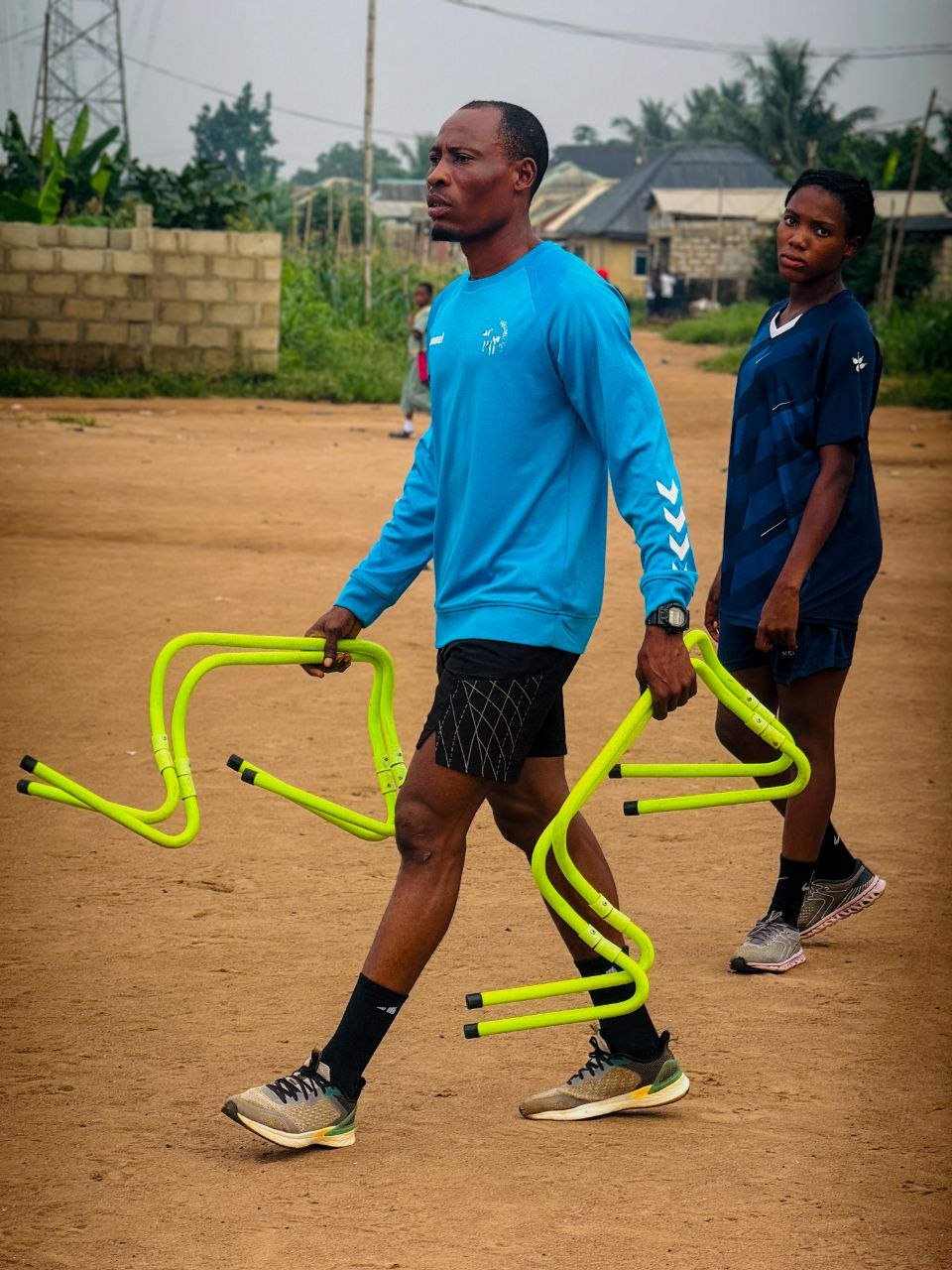 Coach carrying training hurdles across the pitch alongside a BlueWhale player